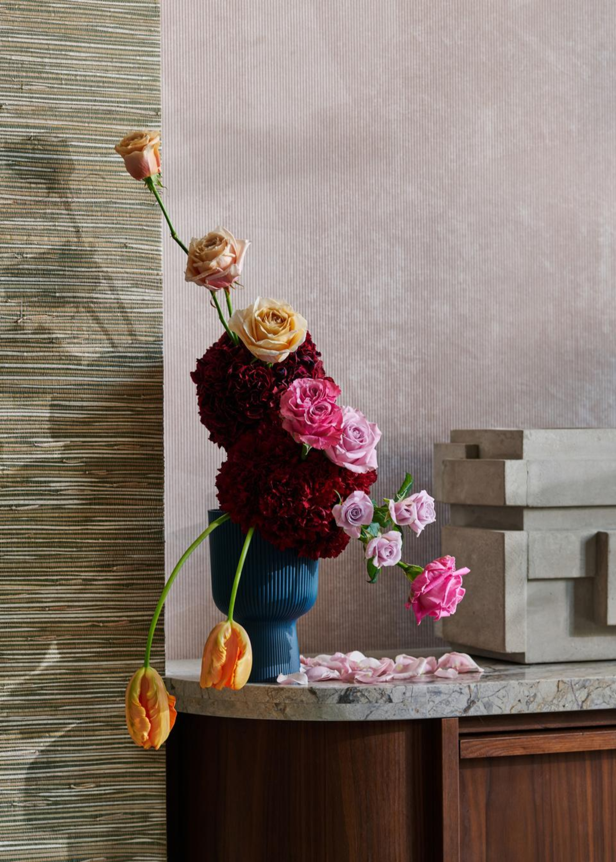 A colorful ribbed vase with oxblood flowers, peach, purple and mauve blooms