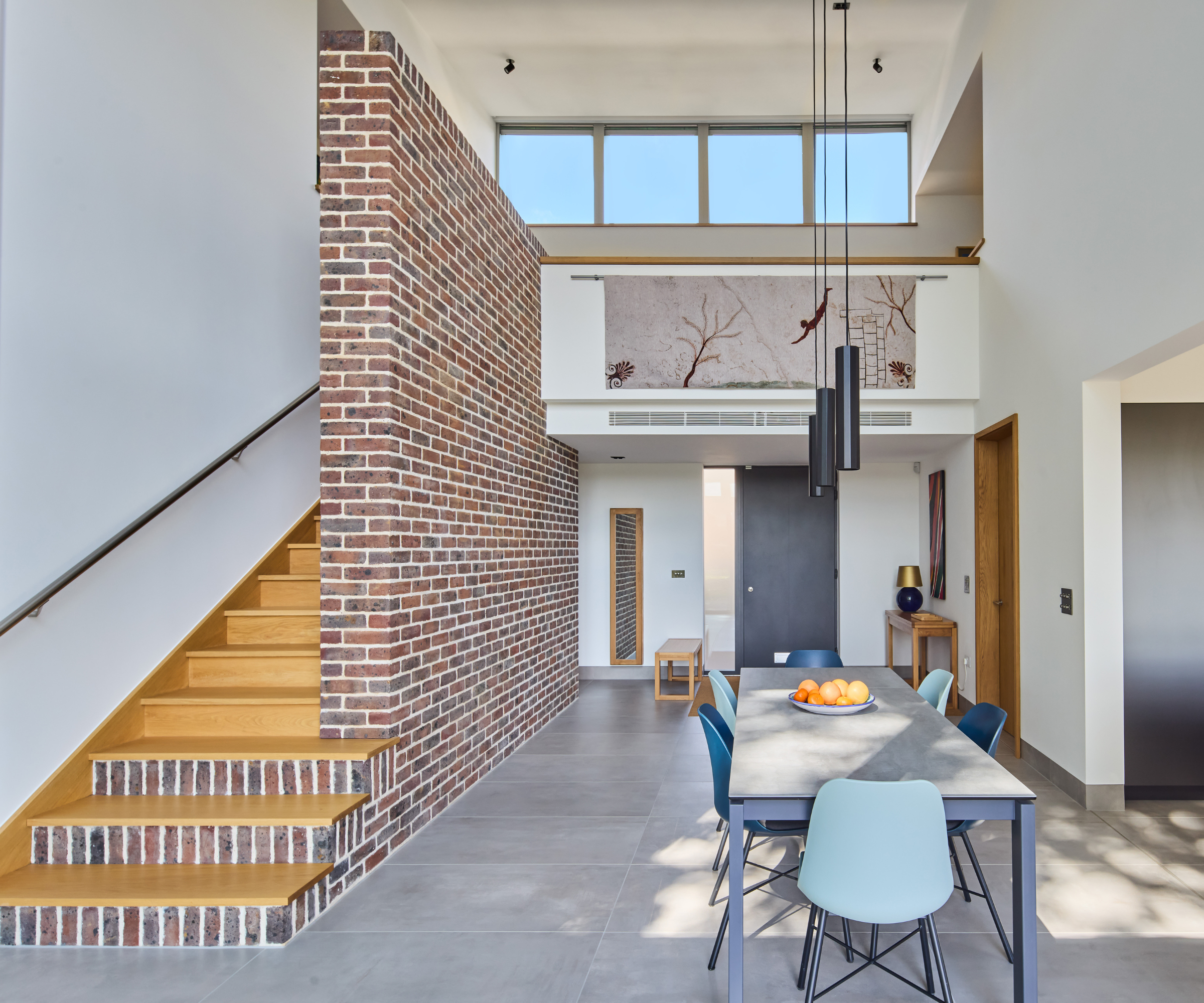 Dining room with front door directly behind in the background and a staircase to the left hand side with red brick wall on the side and stair risers