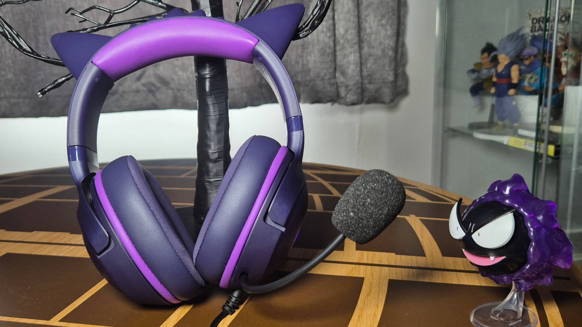 Photo of a purple headset sitting upright on a table with a toy of the Pokemon Gastly sitting to the right.