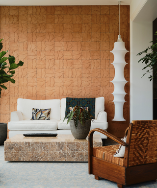 Earthy colored indoor-outdoor space with stone coffee table placed in front of white couch and sculptural light fixture