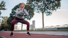 Woman squatting with resistance band around her thighs on outdoors running track