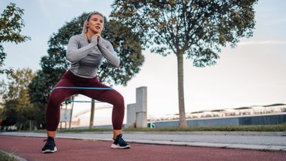 Woman squatting with resistance band around her thighs on outdoors running track