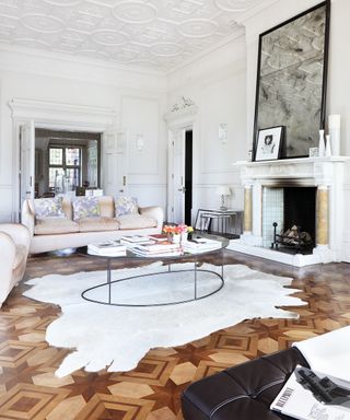 Wooden living room trends illustrated by a large parquet floor in a white living room with pastel sofas.