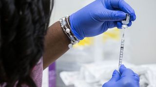 A syringe is filled with Pfizer-BioNTech Covid-19 vaccine by a woman in blue surgical gloves.