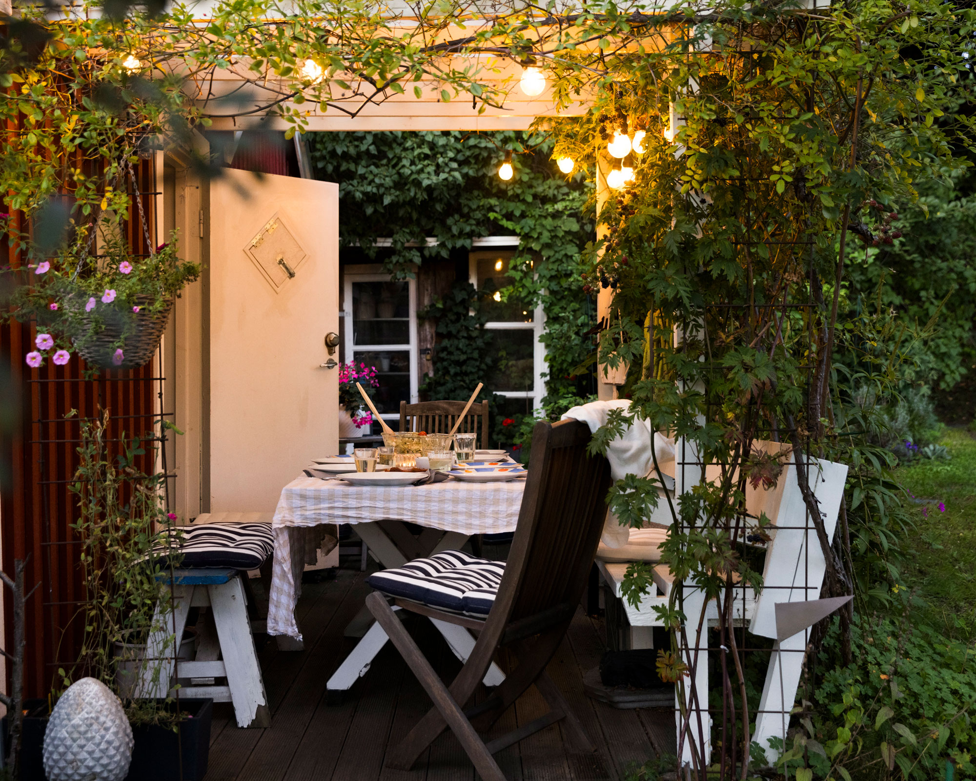 small patio area with lighting, climbing plants and trellis, and outdoor dining with table and chairs