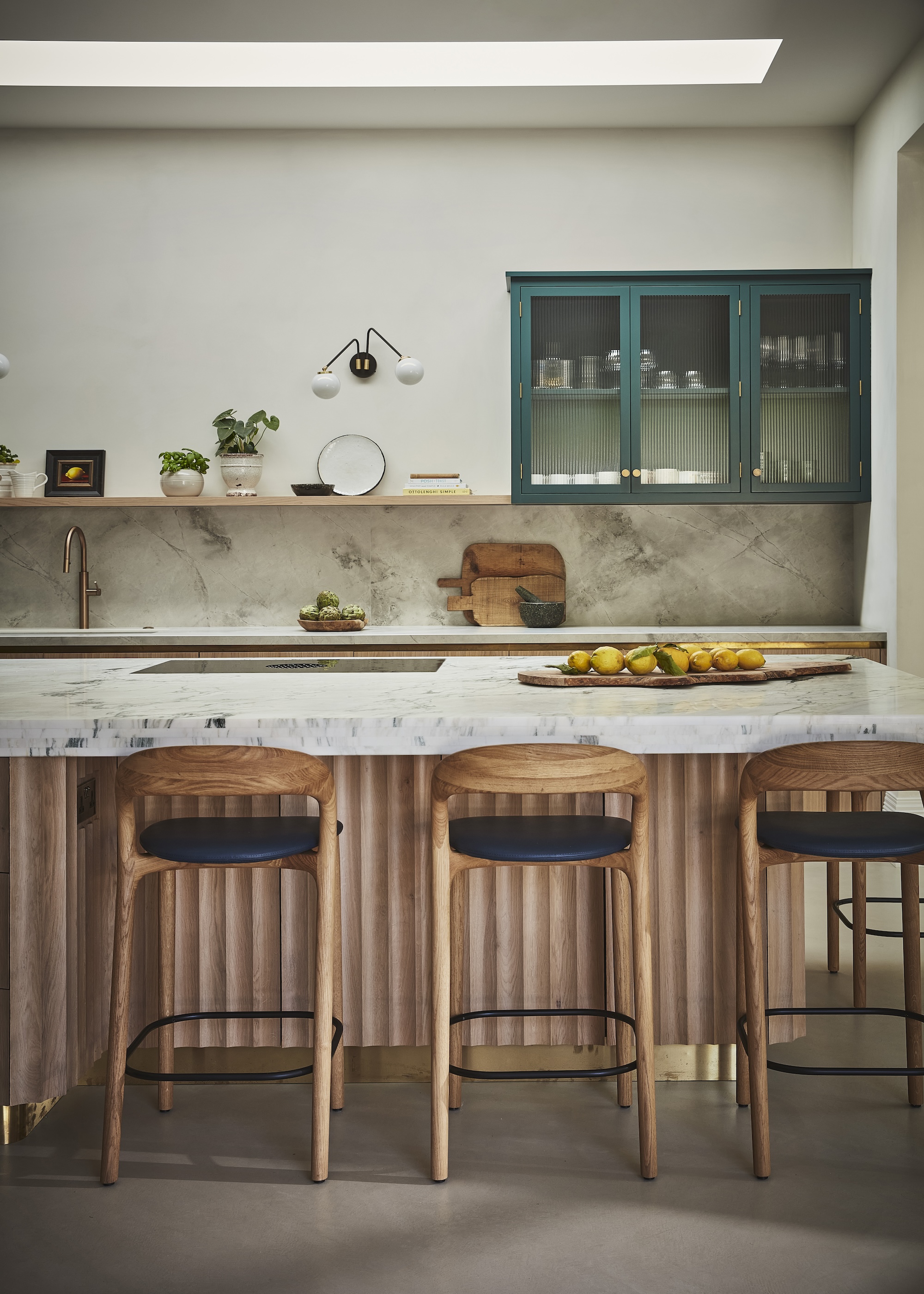 A kitchen island with wide fluted cabinetry in timber with a pale marble worktop and Scandi style bar stools