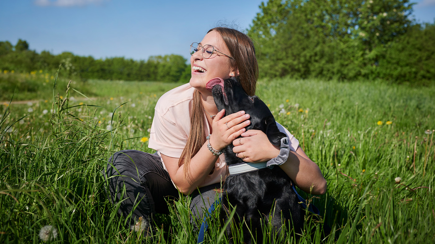 Woman cuddling her black Labrador in a field