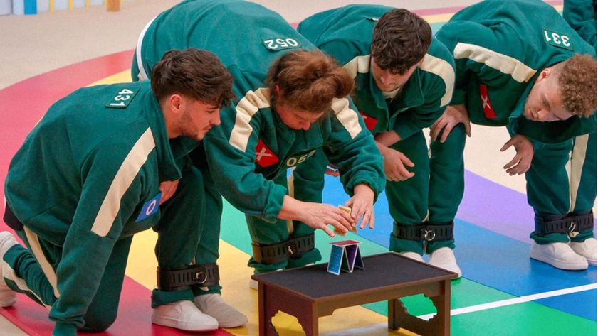 A group of players bend over to watch one place cards on a table