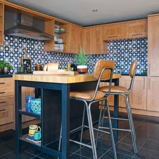Kitchen with wood cabinets, tile stickers, navy kitchen island with leather bar stools
