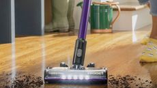 Bissell CleanView XR Pet 300W Stick cordless vacuum vacuuming mud from wooden floor with wellington boots, watering can and person's feet in background