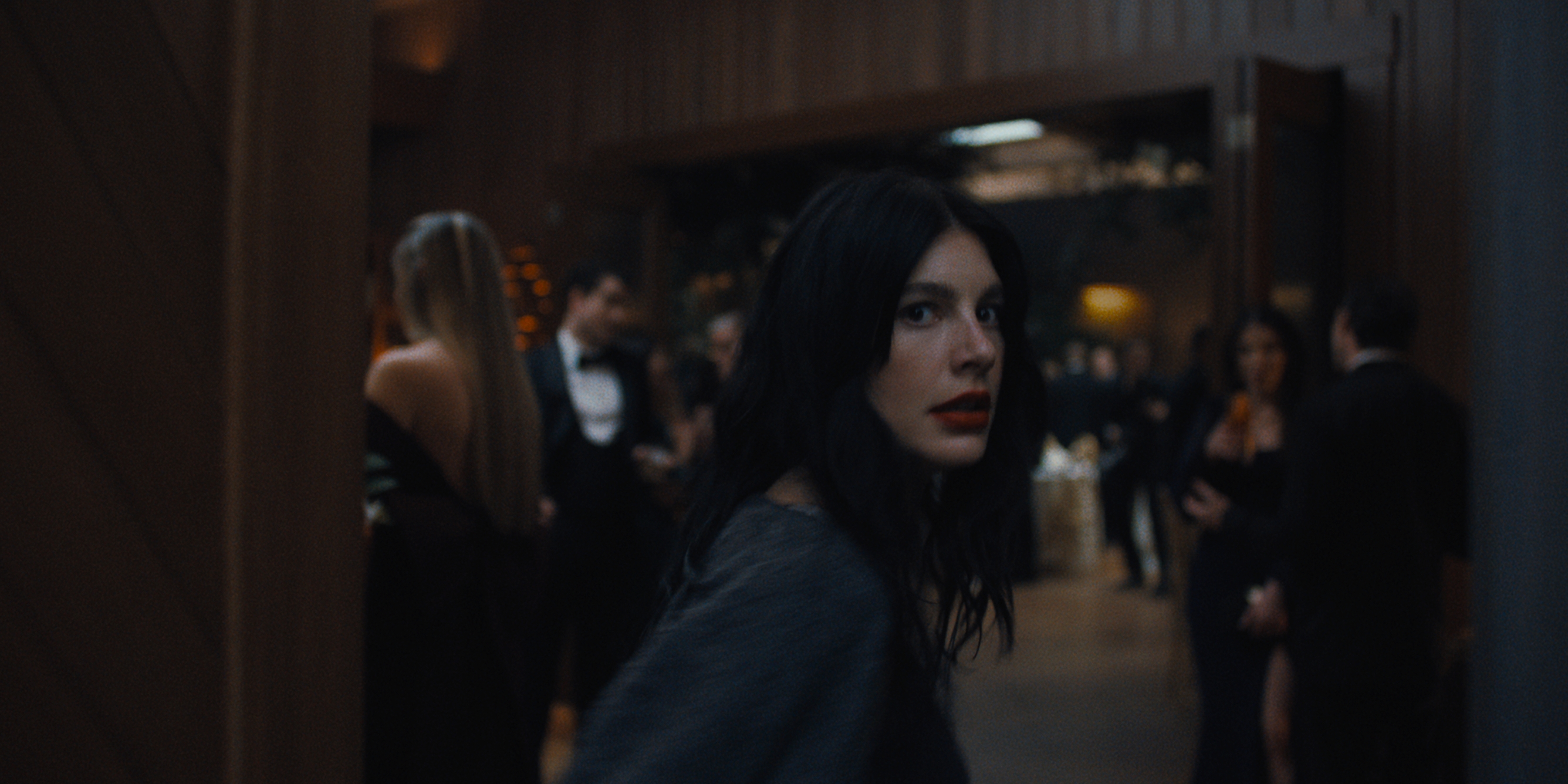 camila Morrone as Rachel Harkin in episode 107 of Something Very Bad Is Going To Happen turning over her shoulder as she walks into a room with a busy party