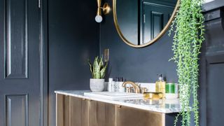 black bathroom trend with metallic gold sink vanity unit, gold round mirror and houseplants