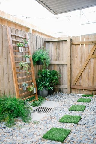 A wooden ladder with potted plants, a wooden fence, and gray pebbles and squares of lawn on the ground