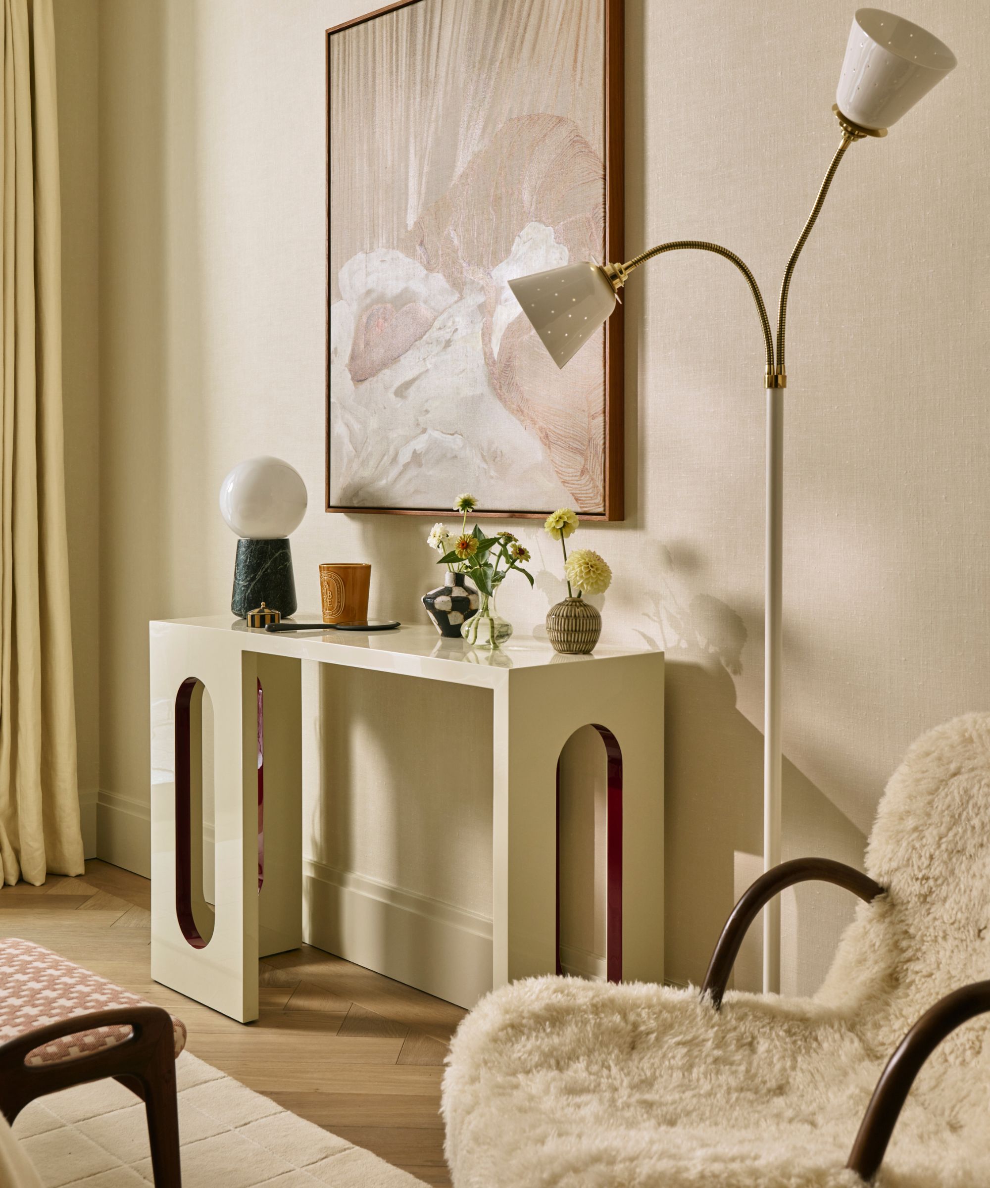 a neutral bedroom corner with a sculptural table and a sheepskin armchair