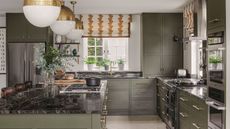 A large green painted kitchen with island. Black marble worktops. 