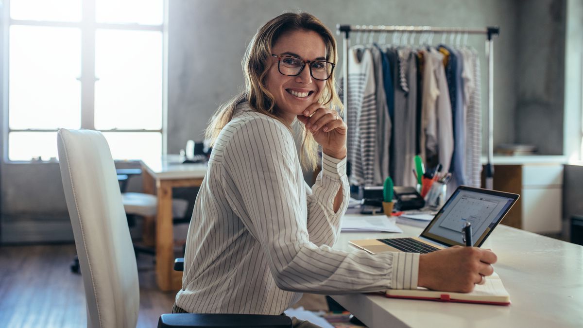 A smiling woman sitting by a desk with laptop