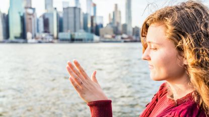 woman in red sweater looking at hand with engagement ring with nyc skyline in the distance, meant to symbolize sologamy