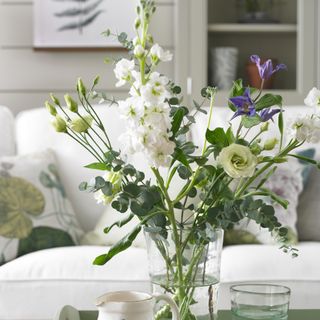 A vase of fresh flowers on a tray on a coffee table in a living room with a sofa in the background
