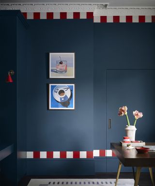 dark blue wall with modern artworks on wall, red and white paint detailing at top and bottom of the wall