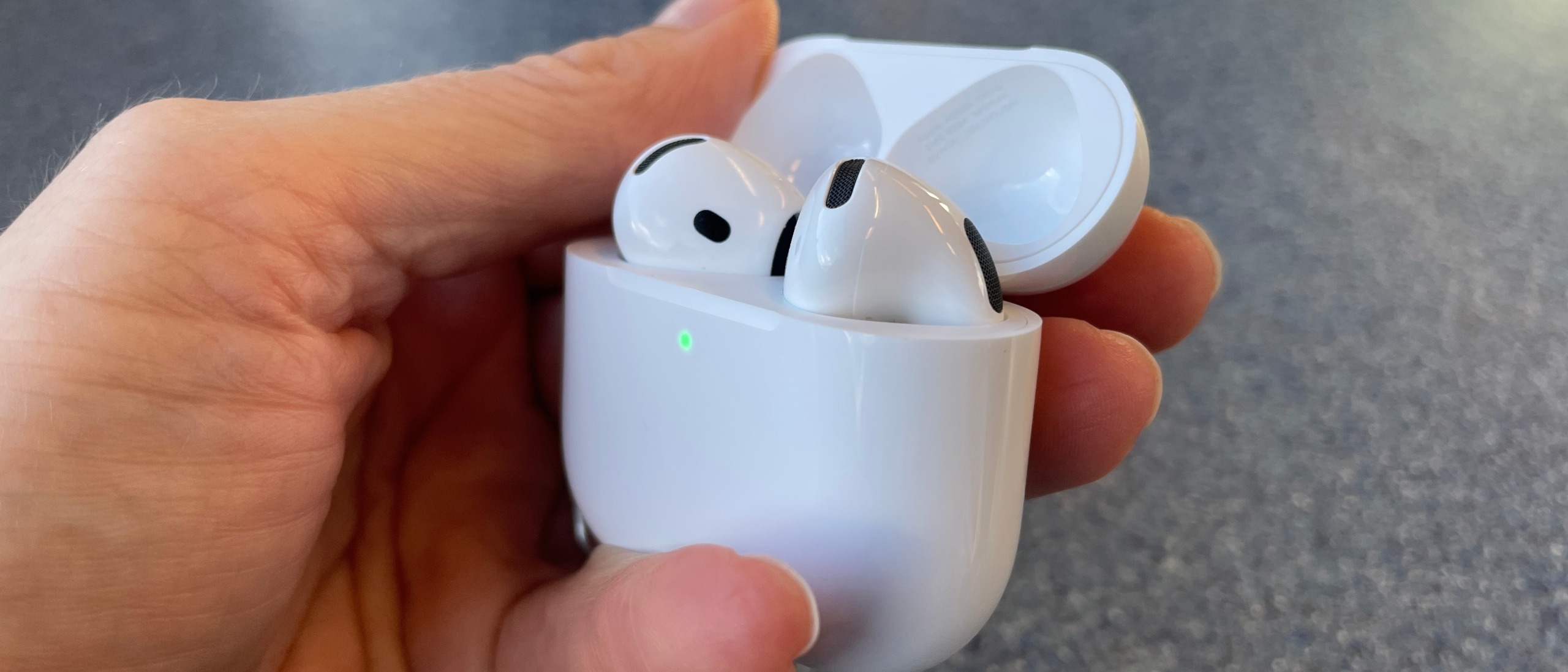 AirPods 5 with Wireless Charging held in a hand, above a blue table