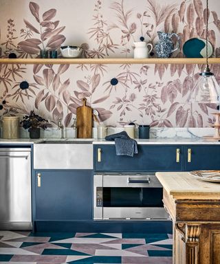 Kitchen with metal and dark blue cupboards, marbled worktop, pink and white floral wall and tiled floor.