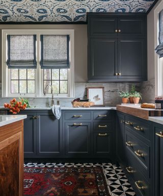 kitchen with dark charcoal cabinets, black and white tiled flooring, patterned wallpaper on ceiling