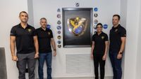 Three men and a woman pose with a wall displays of colorful decals representing different space missions.