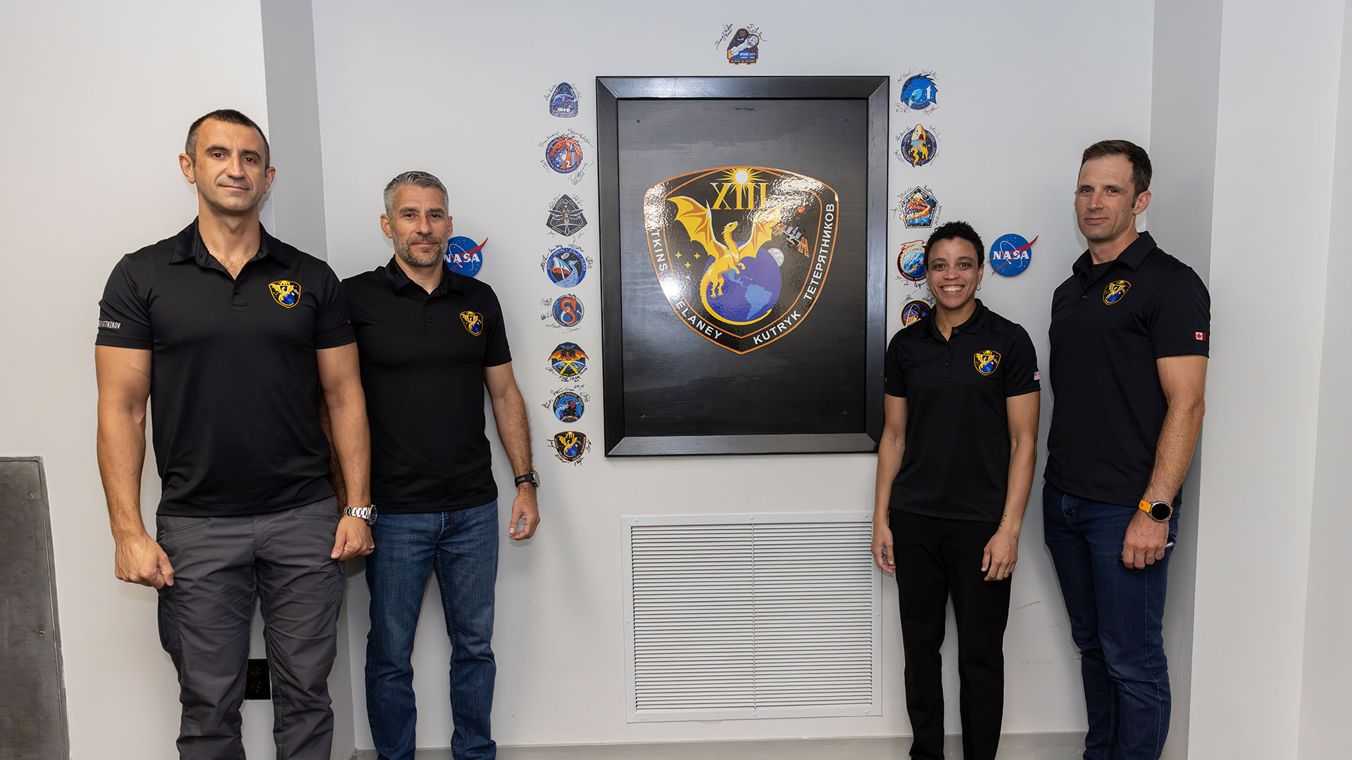 Three men and a woman pose with a wall displays of colorful decals representing different space missions.