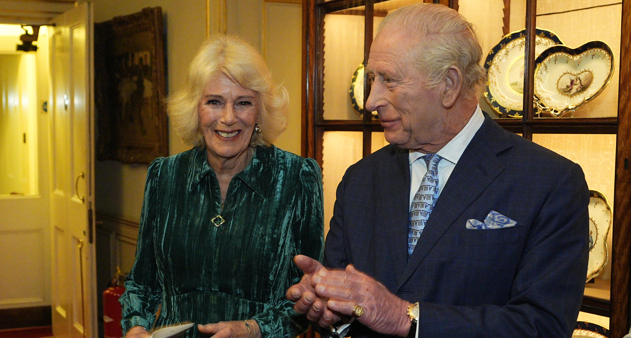 Queen Camilla wearing a green dress standing next to King Charles who is clapping