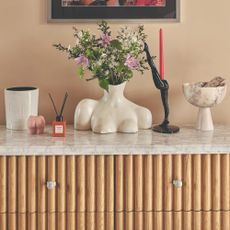 A fluted sideboard with a flower vase, a large Diptyque scented candle and a small reed diffuser along with a few decorative objects