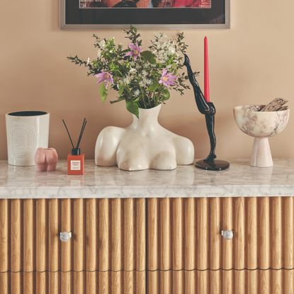 A fluted sideboard with a flower vase, a large Diptyque scented candle and a small reed diffuser along with a few decorative objects