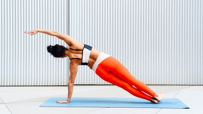 Woman in gym clothes doing a side plank outdoors