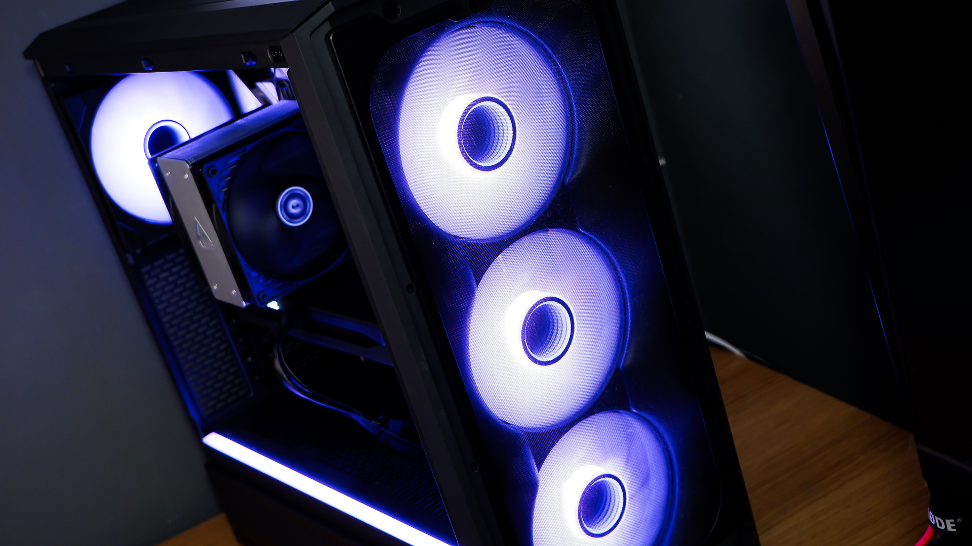 A gaming PC sat on a desk with purple RGB lighting on the fans and light bar enabled.