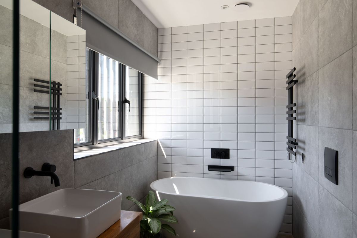Another angle of the white tiled bathroom with large bath and black taps