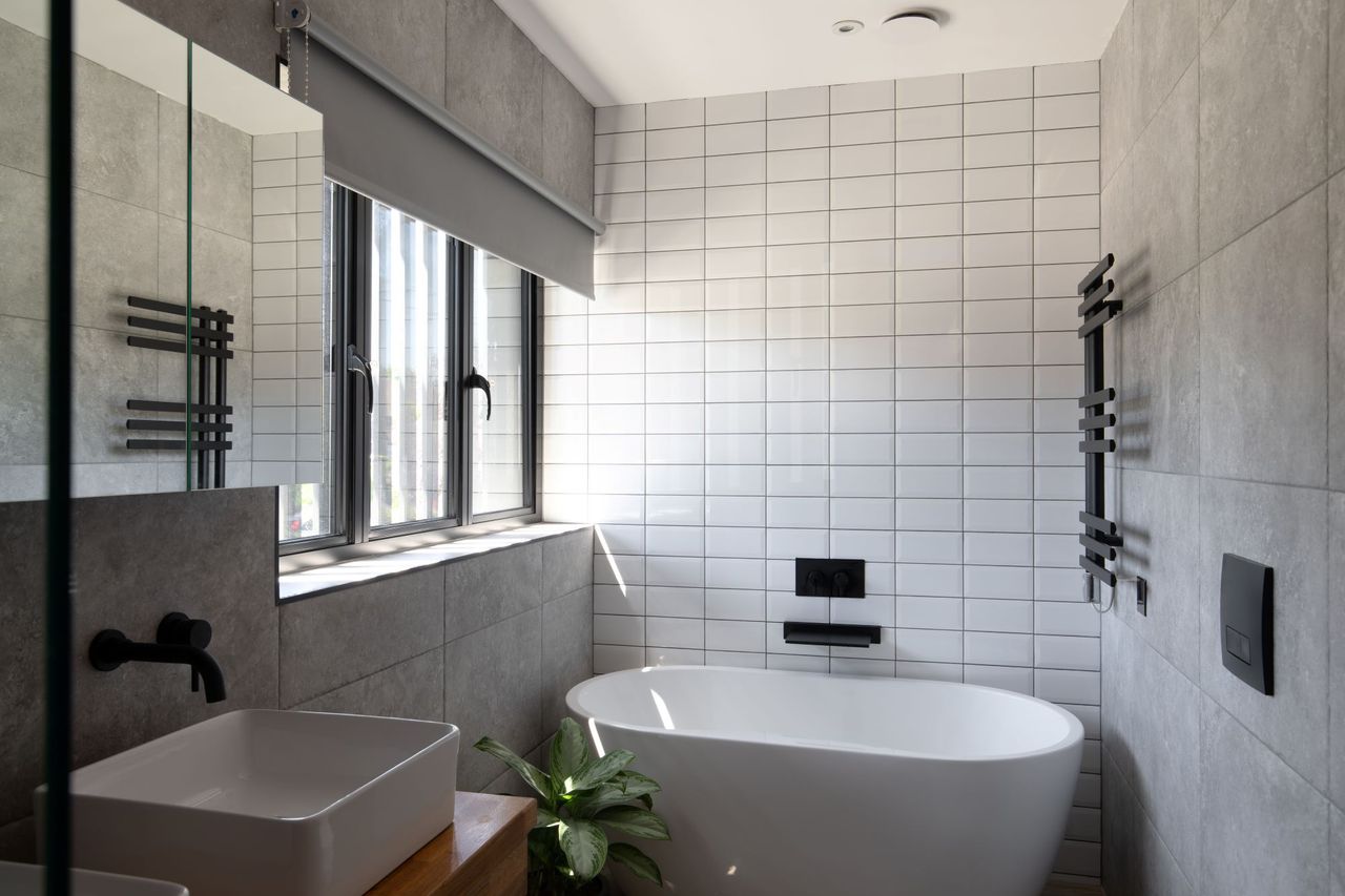 Another angle of the white tiled bathroom with large bath and black taps