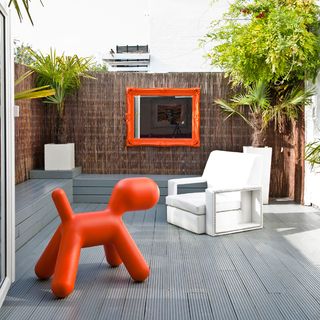 decked garden with red sculpture and white chair