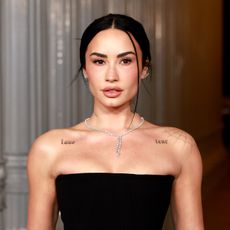 a white woman with dark hair pulled back into a bun wearing a black, strapless dress on a red carpet