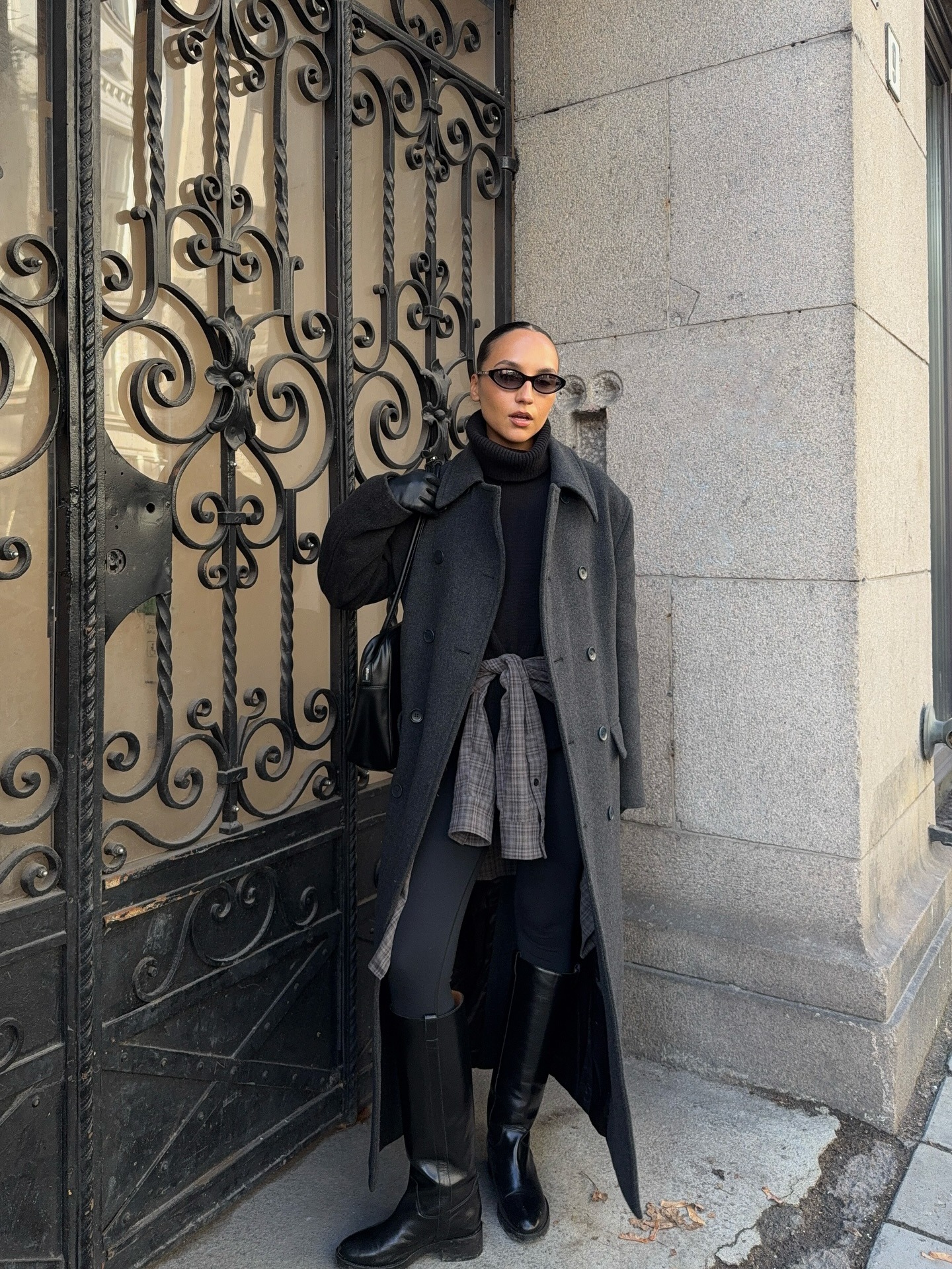 Influencer @ingridedvinsen wears a dark grey coat with leggings, knee-high boots and a checked shirt tied around her waist.