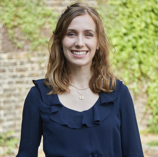 A headshot of a woman with auburn hair in a blue shirt smiling at the camera