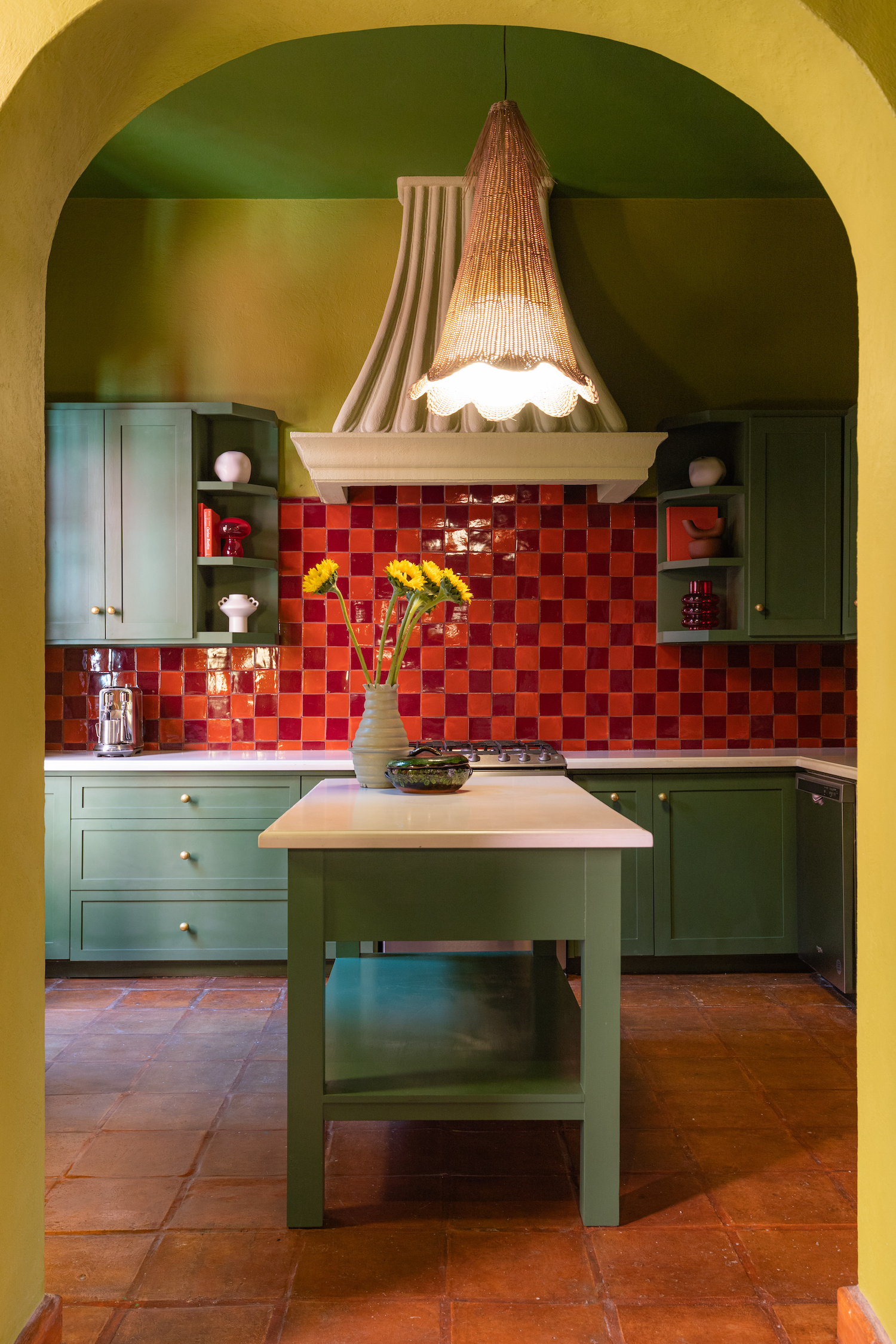 A colorful kitchen with green cabinets and a bright red tiled backplash.