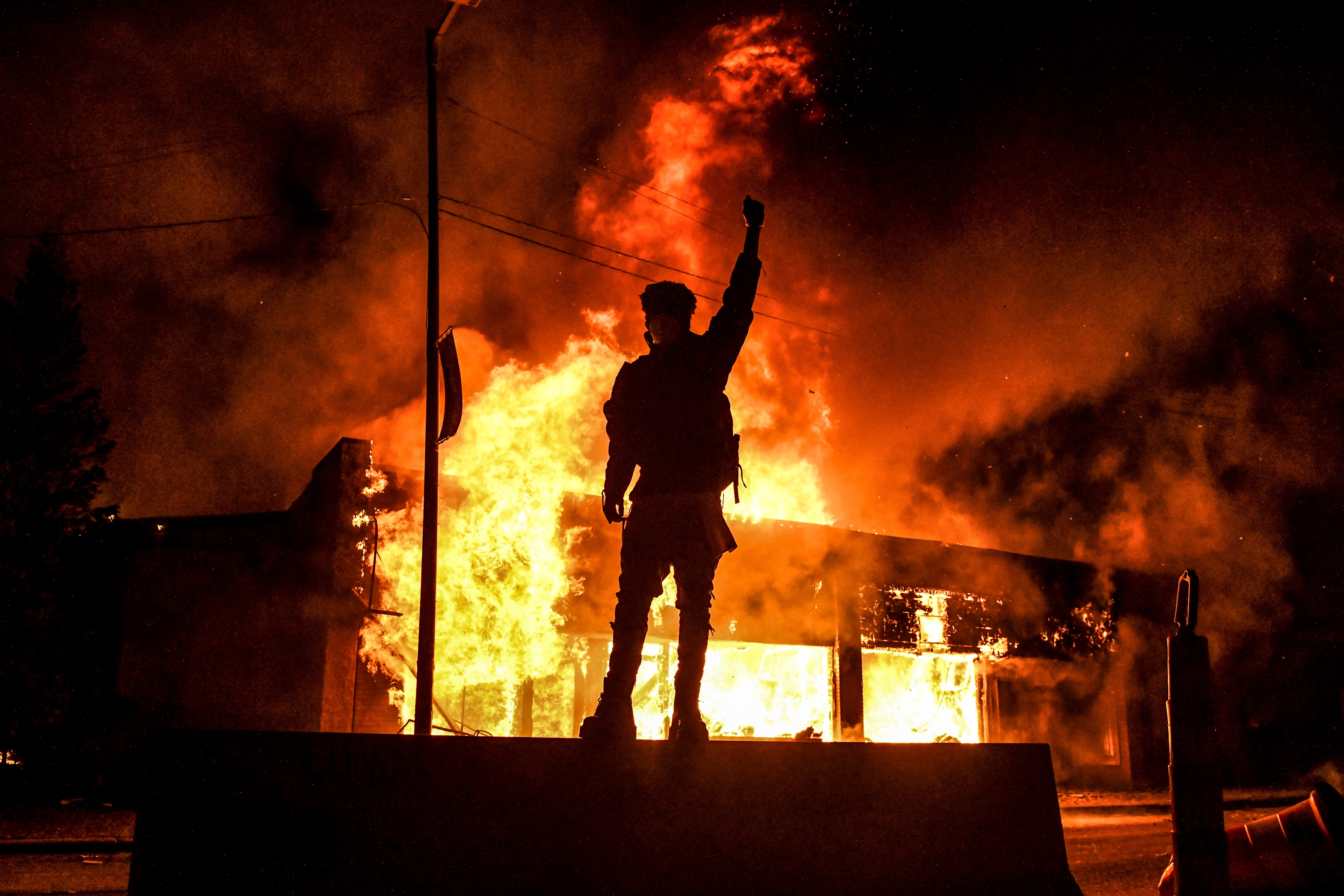 A protester reacts standing in front of a burning building set on fire during a demonstration in Minneapolis, Minnesota, on May 29, 2020, over the death of George Floyd, a black man who died after a white policeman kneeled on his neck for several minutes. Violent protests erupted across the United States late on May 29 over the death of a handcuffed black man in police custody, with murder charges laid against the arresting Minneapolis officer failing to quell seething anger. (Photo by Chandan KHANNA / AFP) (Photo by CHANDAN KHANNA/AFP via Getty Images)