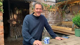 Monty Don wearing a navy jumper and drinking a cup of tea in the garden for Gardeners' World 2023. 