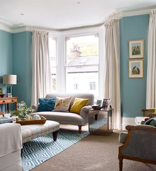Blue living room with grey sofa, gemoetric rug and heavy curtains in a bay window