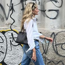 @elizagracehuber wearing a white button-down shirt and Levi's jeans with a brown bag and gold earrings.