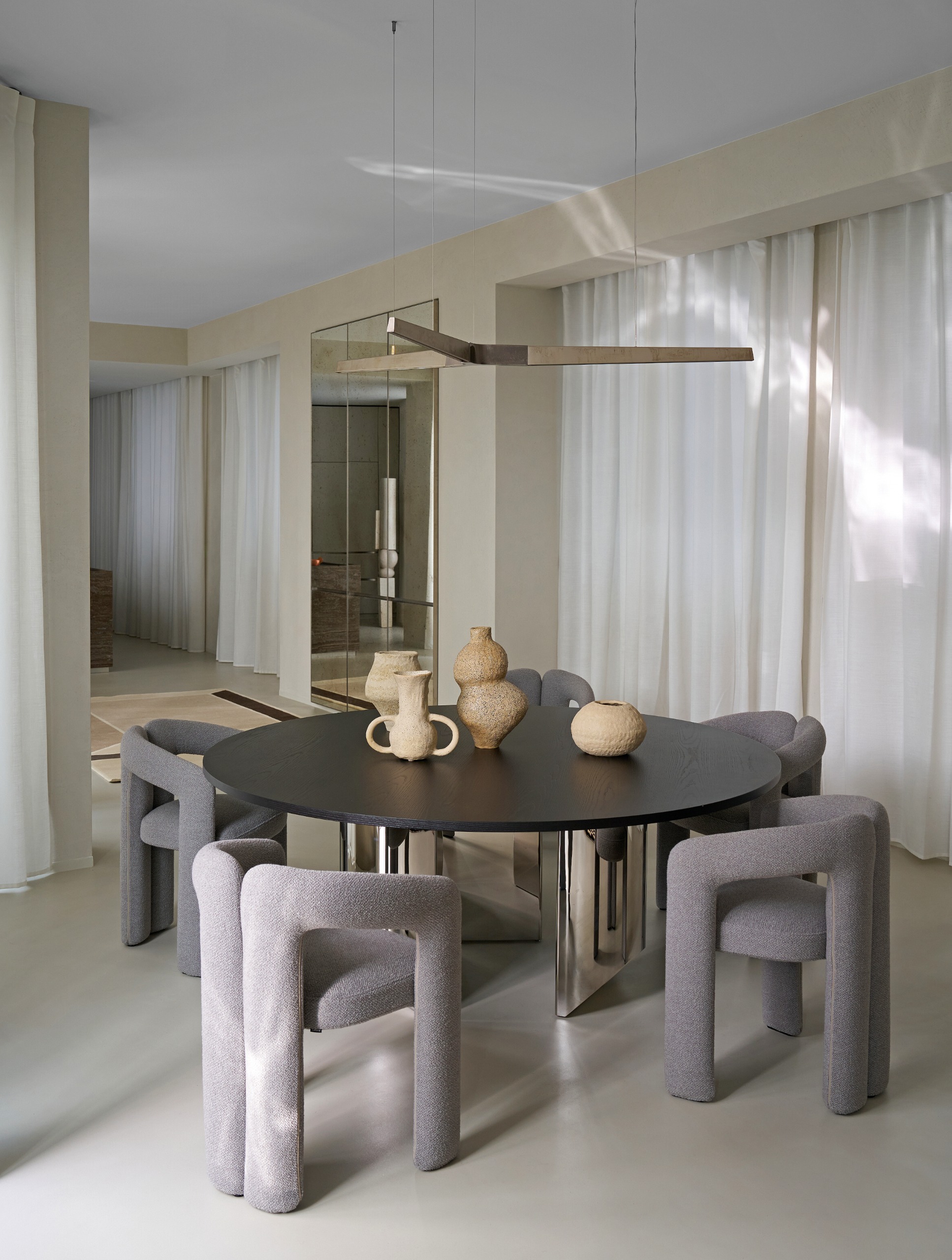 Dining room with grey concrete floor, black round dining table with chrome legs, purple-grey velvet dining chairs and chrome pendant light