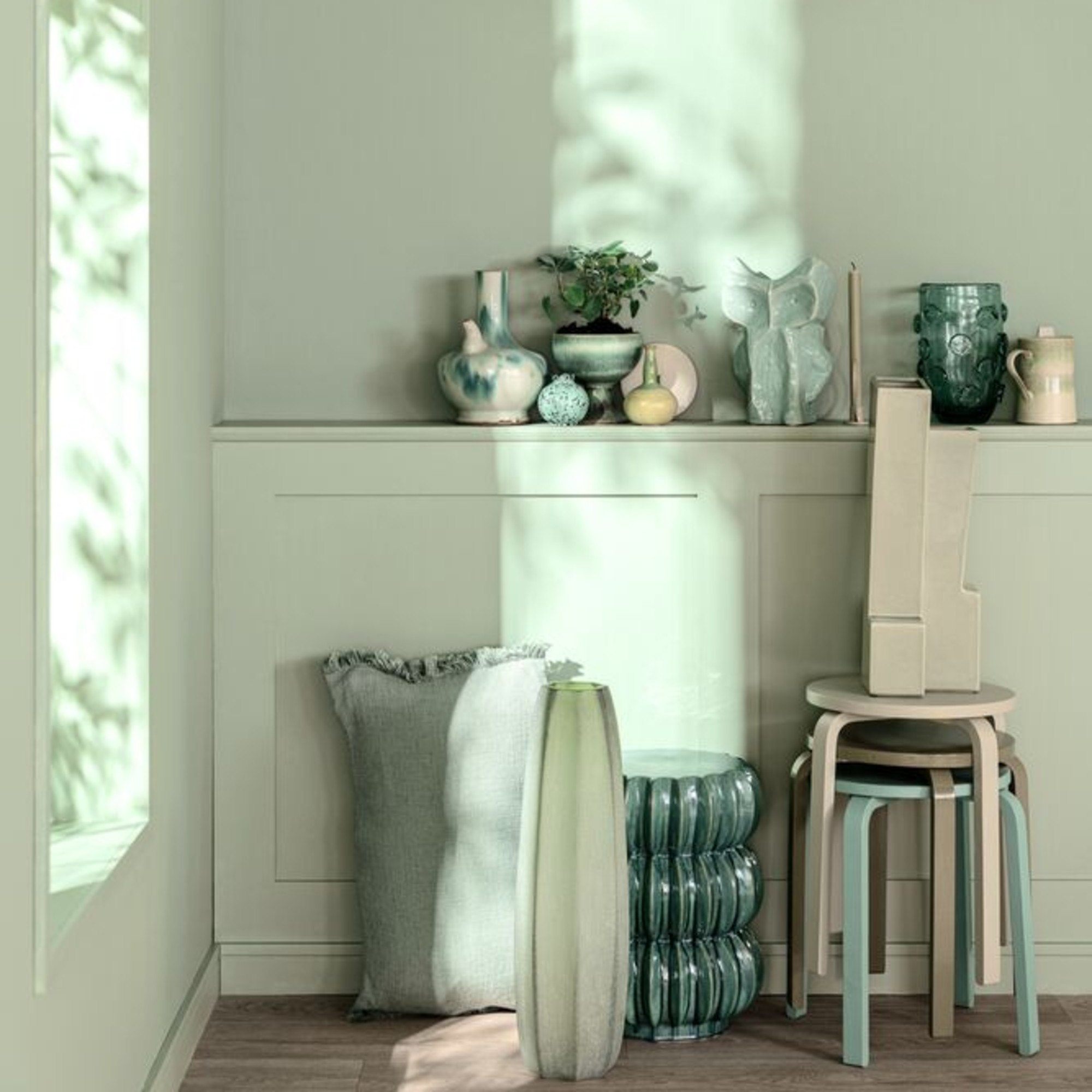 A room colour-drenched in Dulux's Soulful Sage paint shade with decorative objects displayed on a shelf and wooden stools stacked on top of each other