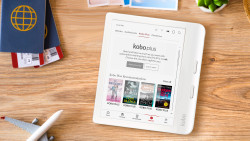 A white digital e-reader displaying kobo plus on a wooden table with a passport and model plane 