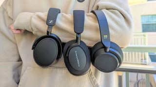 3 black headphones draped over writer's arm for best underrated noise-cancelling headphones feature