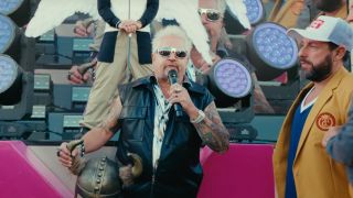 Guy Fieri speaks to the crowd while Adam Sandler watches on in Happy Gilmore 2.