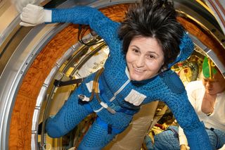 astronaut samantha cristoforetti floating in an airlock and wearing a blue garment that goes underneath a spacesuit